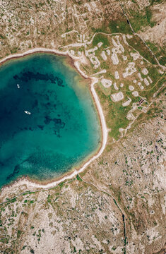 Aerial view of turquoise waters meet the rugged coastline, contrasting with the dry, arid landscape dotted with sparse greenery, Baska, Primorje-Gorski Kotar County, Croatia.