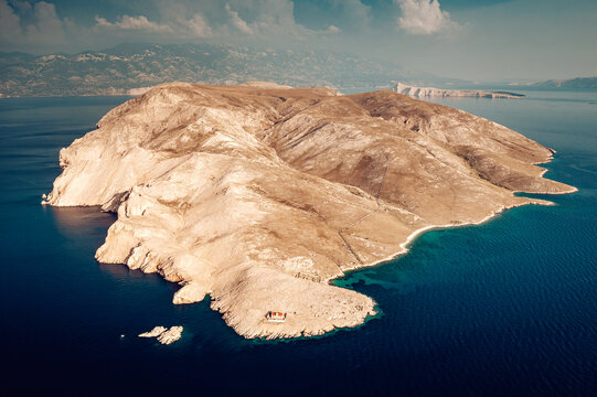 Aerial view of a stark, sun-drenched island rises majestically from the deep blue Adriatic Sea, its rocky terrain contrasting with the clear waters, Baska, Primorje-Gorski Kotar County, Croatia.