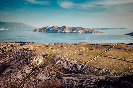 Aerial view of a rugged, sun-drenched landscape meets the tranquil turquoise sea, an island sits peacefully on the horizon, Baska, Primorje-Gorski Kotar County, Croatia.