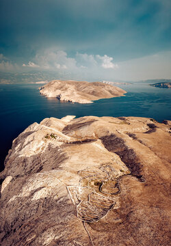 Aerial view of arid, rocky foreground leading to the deep blue sea and distant island under a cloudy sky, Baska, Primorje-Gorski Kotar County, Croatia.