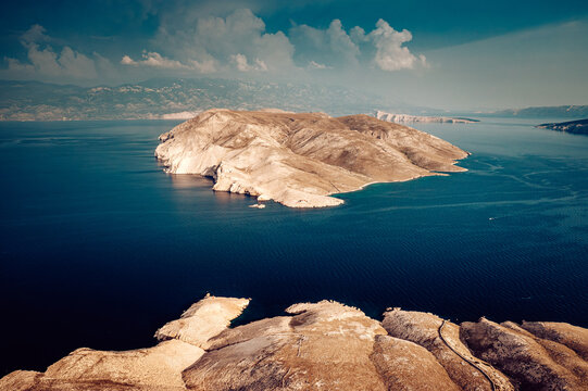 Aerial view of rugged and arid island contrasting against the deep blue sea under a cloudy sky, Baska, Primorje-Gorski Kotar County, Croatia.