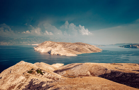 Aerial view of the arid landscape meets the tranquil turquoise sea, punctuated by rocky islets under a vast sky, Baska, Primorje-Gorski Kotar County, Croatia.
