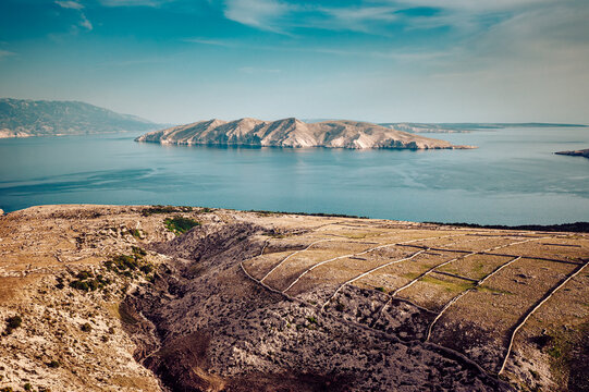 Aerial view of arid landscape meets the tranquil sea, with a distant island adding depth to the horizon, Baska, Primorje-Gorski Kotar County, Croatia.