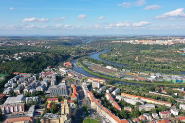 Fototapeta premium Aerial view of Prague with the Vltava River flowing through Dejvice, showing urban districts, green hills, and wastewater treatment plant under clear sky.