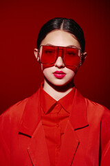 Fashion model posing with distinctive oversized red sunglasses and a stylish red blazer against a...