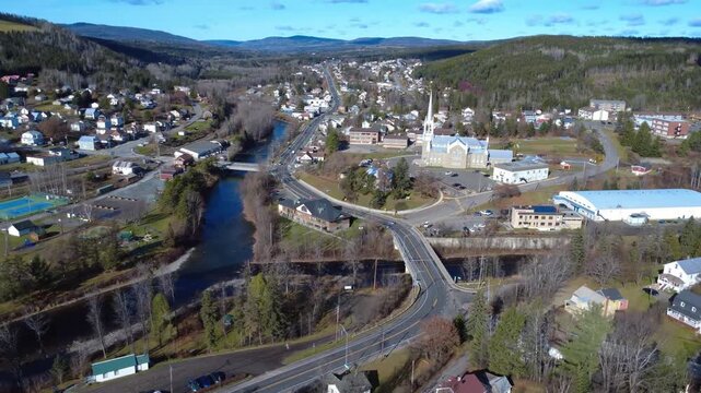 Autumnal flyover of the small riverside town of Causapscal, with a pass near the church steeple next to the public school. Matapedia Valley, Quebec, Canada, 2025.