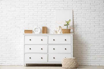 Old books, picture and vases on chest of drawers near white brick wall in room