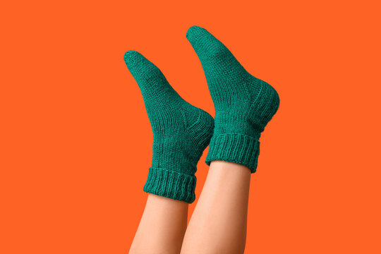 Legs of young woman in green knitted socks on orange background