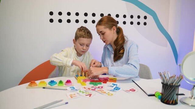 Female speech therapist working with a little boy learning letters and shapes