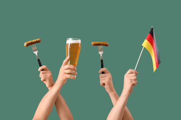 Male hands with glass of cold beer, Germany flag and traditional sausages on green background....