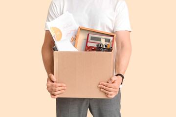 Fired young man holding box with personal stuff on beige background, closeup