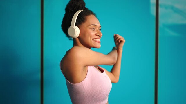 Smiling woman stretching after outdoor workout, raising arm with headphones on, enjoying music and movement, urban fitness lifestyle, positive energy, motivation, wellness routine ow