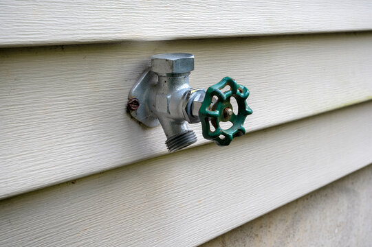 Outdoor water faucet mounted on house exterior wall. House water tap outside