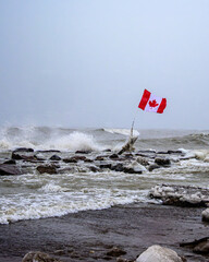 Obraz premium Vertical view of a Canadian flag fluttering in intense winter wind above a rough Lake Ontario.