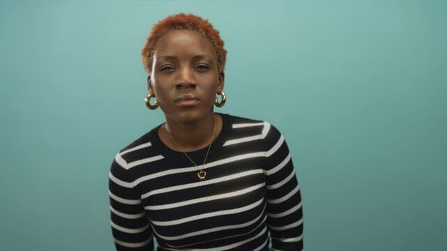 Woman tilts head revealing face with closed eyes and hoop earrings in striped top in studio; calm introspection.