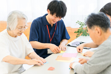 Elderly people and male and female caregivers doing origami in a group home or nursing home