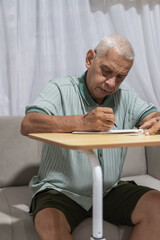 Routines senior man writing notes on notebook in living room