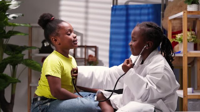 African girl children role-playing doctor and patient with stethoscope during pediatric visit in clinic