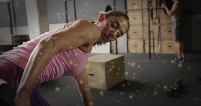 Woman bracing floor hand and pulling hex dumbbell in gym, golden specks accenting strength building