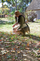Woman wearing hat crouching petting tabby cat in garden