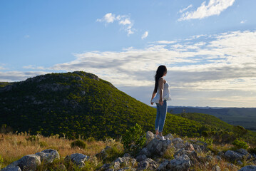Woman standing on rocky hill viewing mountain landscape