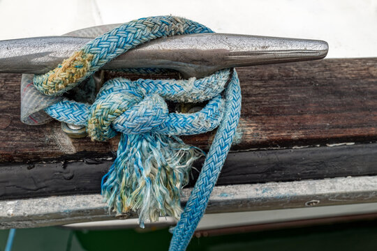 A frayed blue rope tied to a boat cleat on a vessel