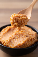Scooping traditional Japanese miso paste from a black bowl with a wooden spoon, fermented soybean...