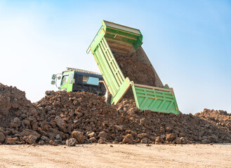A green tipper truck unloading a large mound of brown soil at a land development site.