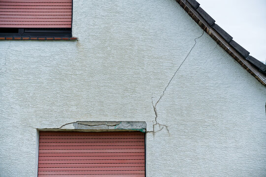 Two story house with closed shutters and visible wall crack