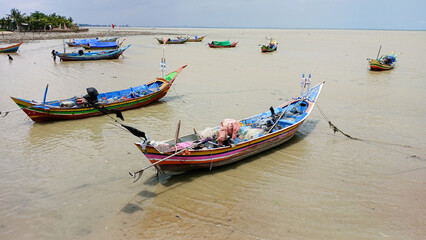 Obraz premium Fishing boats are anchored along the shore, their colorful boats floating on the murky brown water.
