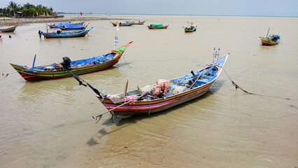 Obraz premium Fishing boats are anchored along the shore, their colorful boats floating on the murky brown water.