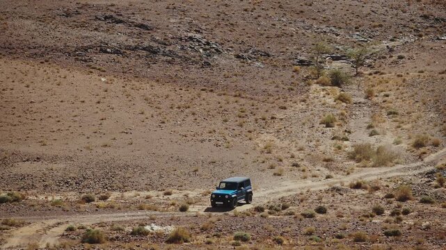 Off road vehicle driving through arid Moroccan desert terrain under clear sky, medium telephoto overview rocking over road