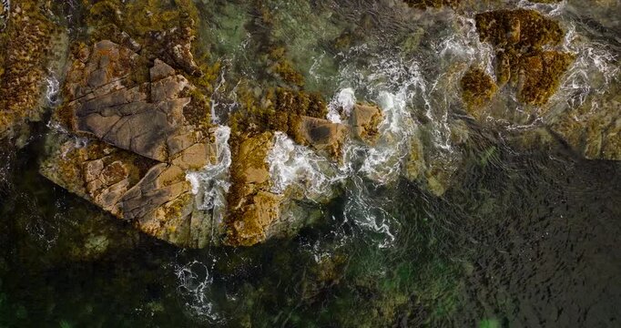 Rugged coastline with clear green and dark water revealing underwater rocks and seaweed in &Aring;rnessan, Norway. Aerial top-down ascending