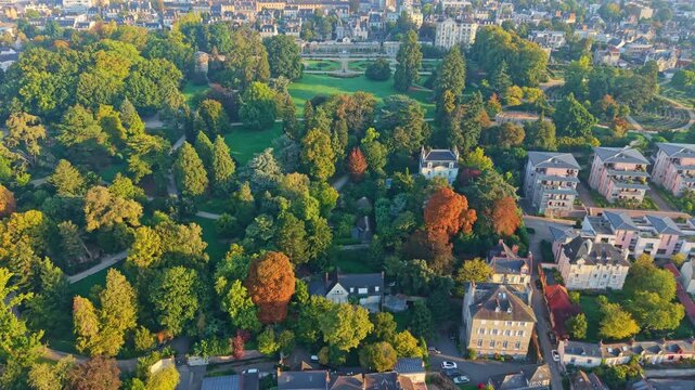 Wide aerial pullback Parc du Thabor with dense tree canopy and autumn colors in Rennes, golden hour establish
