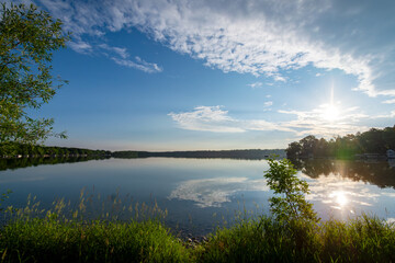 Lush green shoreline of a Waukesha County lake in early June. Bright morning sun reflects on calm Wisconsin water under blue skies.