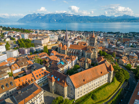 Aerial view of Lausanne Cathedral surrounded by historic rooftops, with Lake Geneva and alpine mountains in the background in Lausanne, Switzerland