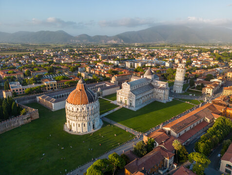 Wide aerial view of Pisa Piazza dei Miracoli at sunset featuring the Leaning Tower, Cathedral and Baptistery in warm evening light