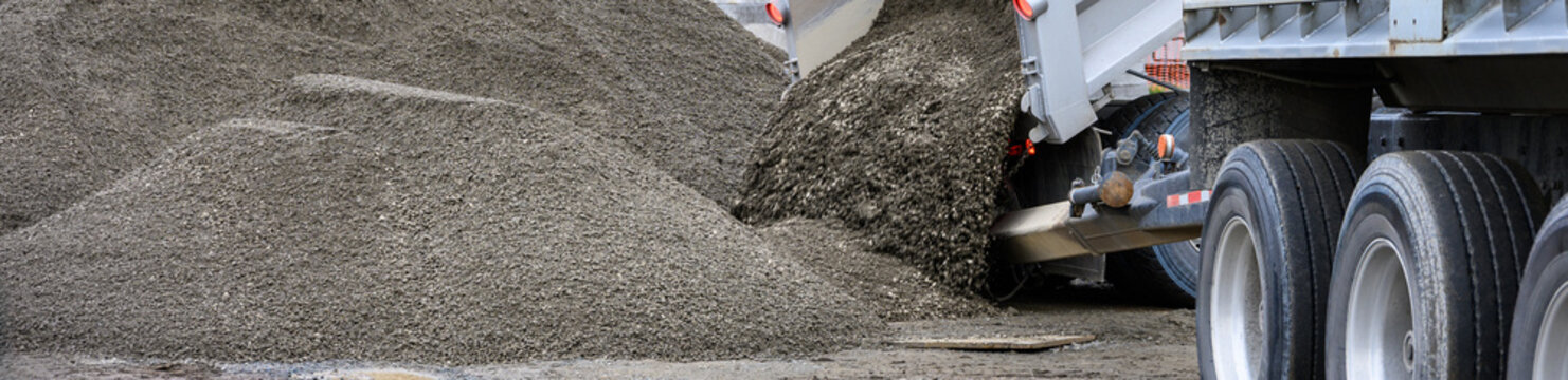 Construction dump truck trailer unloading gravel with a hydraulic lift bed spilling material onto the ground, as a job site 
