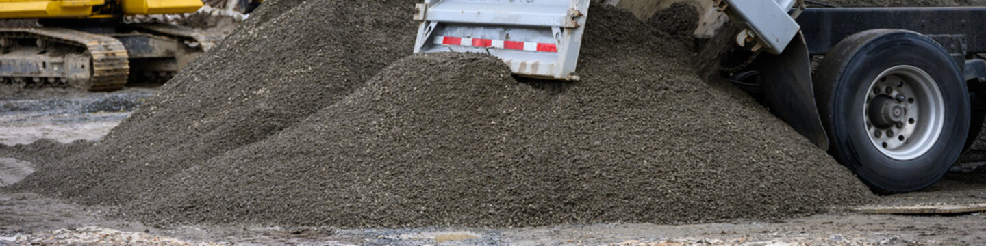 Construction dump truck unloading gravel with a hydraulic lift bed spilling material onto the ground, as a job site 
