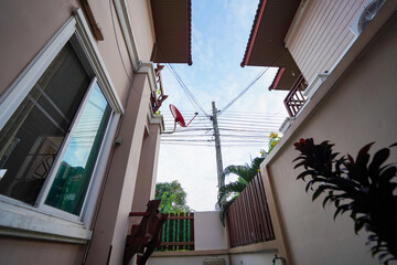 Naklejka premium Low angle view of modern beige house exterior with wooden balcony and wall lamp framed by green leaves