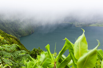 Obraz premium Volcanic lake surrounded by lush greenery in Sete Cidades crater. Mist partially covers the landscape. View from elevated point in San Miguel, Azores.