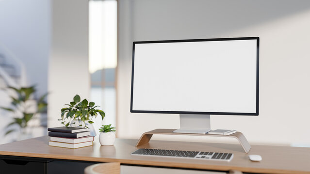 White screen computer with books and potted plants on wooden table across wall in modern style room.