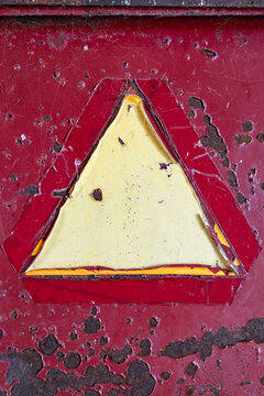 A weathered Slow-Moving Vehicle (SMV) sign on a rusty, peeling red metal