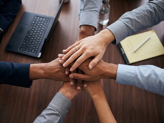 Obraz premium Diverse business colleagues stacking hands on wooden conference table for teamwork and strong unity