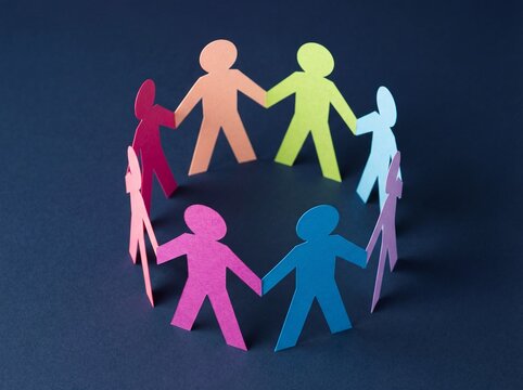 Colorful paper figures holding hands in a circle on dark blue background symbolizing diversity