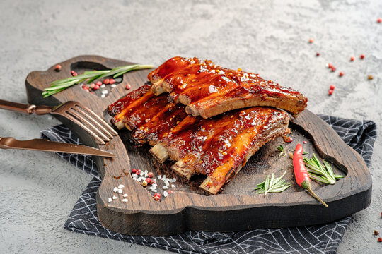 Glazed barbecue pork ribs with sticky sauce, served on rustic wooden board with fresh rosemary and red chili garnish. Juicy grilled spare ribs, gourmet meat dish, appetizing dinner or party food