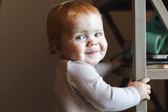 young one year old boy with red hair smiles over his shoulder