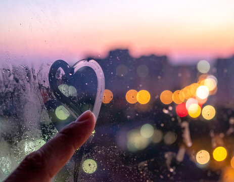 Romantic heart drawn on a steamy window at sunset with bokeh lights