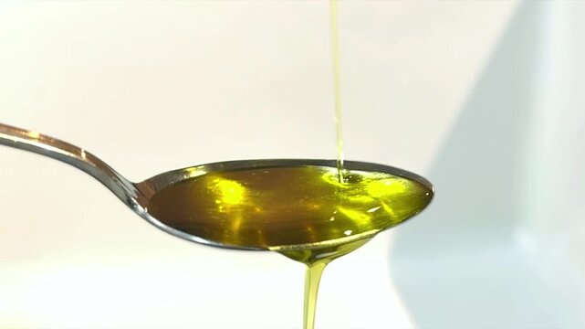 close up of olive oil being poured slowly onto metal spoon with white background