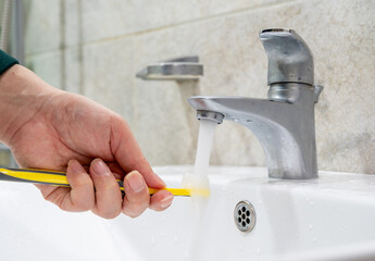 Rinsing toothbrush under running water in bathroom sink, daily oral hygiene concept